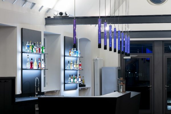 Glas-Pendelleuchten in lila leuchtend nebeneinander hängend über einer Bar